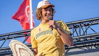 Der Surfer Lennart Neubauer hält eine Trophäe und ein Mikro in der Hand.