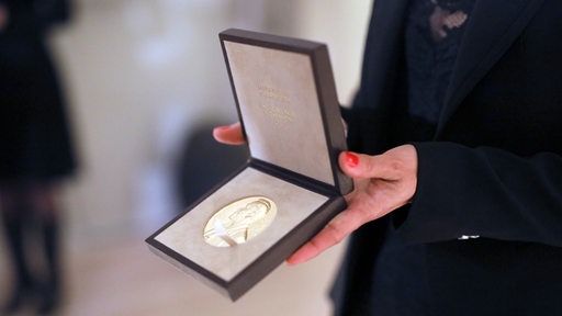 Nahaufnahme: Die Nobelpreis-Medaille wird von einer Frau in die Kamera gezeigt.