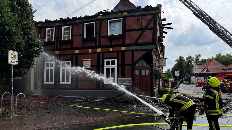 Feuerwehrleute stehen vor einem ausgebrannten Gebäude und halten einen Feuerwehrschlauch auf das Haus