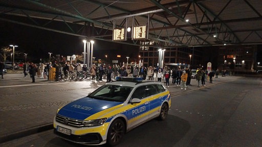 Ein Polizeiauto steht vor einer Menschenmenge an einem Bahnhof