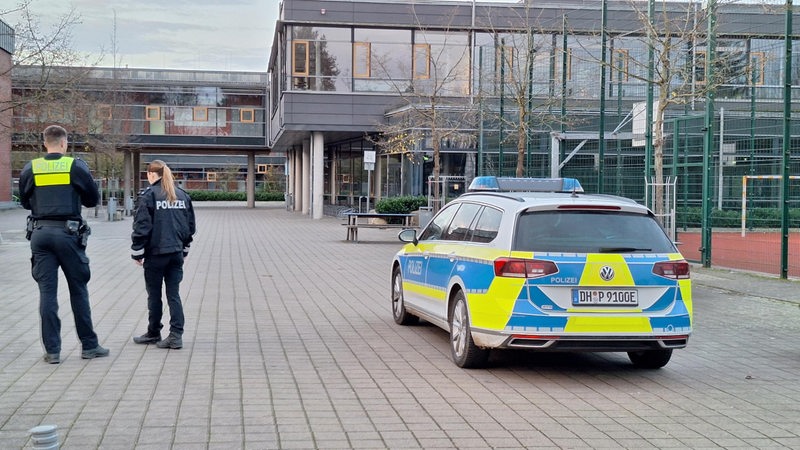 Eine Polizistin und ein Polizist stehen auf einem Schulhof.