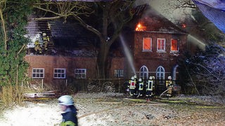 Feuerwehrmänner versuchen ein großes altes Bauernhaus zu löschen, welches in Flammen steht.