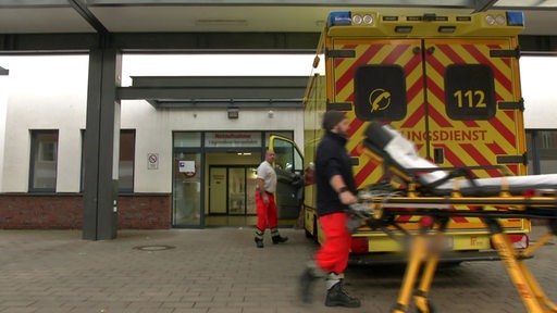 Ein Rettungssanitäter fährt eine Trage vor einen Rettungswagen.