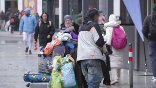 Ein Obdachloser schiebt einen voll bepackten Einkaufswagen