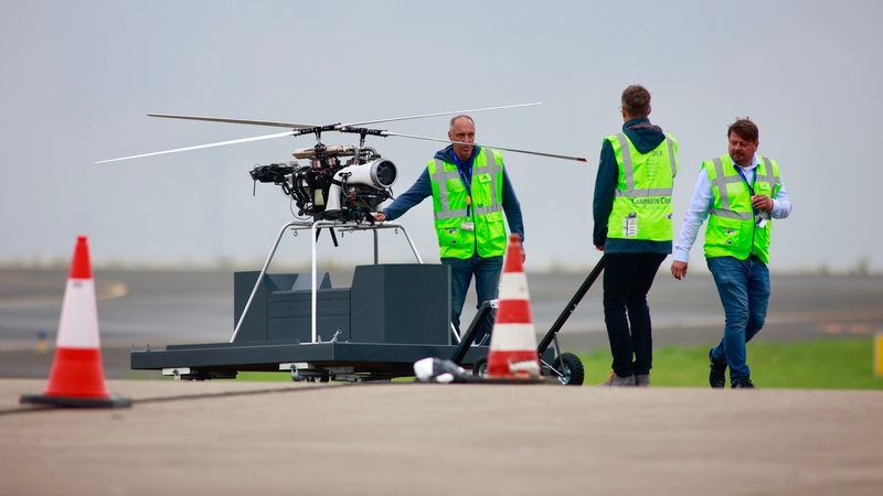 Drei Männer in Warnweste stehen neben einer großen Drohne.