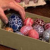 Eine Hand legt verzierte Eier in eine Schale