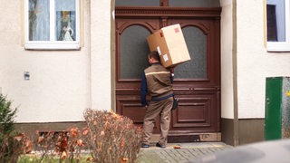 Ein Paketbote von UPS bringt ein großes Paket und wartet damit an einer Haustür.