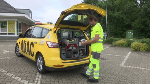 Björn Lüthje KFZ Mechaniker steht neben seinem ADAC-Wagen. 