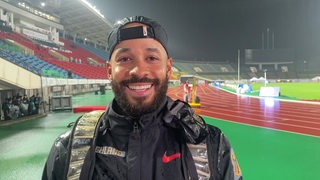 Para-Weitspringer Leon Schäfer strahlend im strömenden Regen im Stadion nach dem Gewinn von WM-Gold beim Interview.