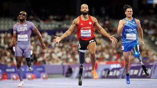 Para-Sprinter Leon Schäfer breitet nach dem Sieg im Vorlauf selbstbewusst die Arme aus nach der Ziellinie.