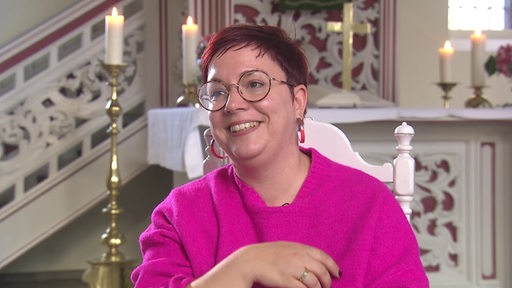 Eine Person in pinker Kleidung sitzt vor einem Altar, auf dem einige Kerzen brennen