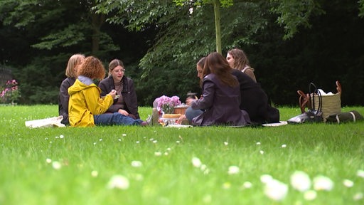 Mehrere junge Menschen picknicken gemeinsam in einem Park.