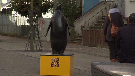 Eine Pinguinskulptur steht auf einer gelben Box mit einem QR-Code darauf.