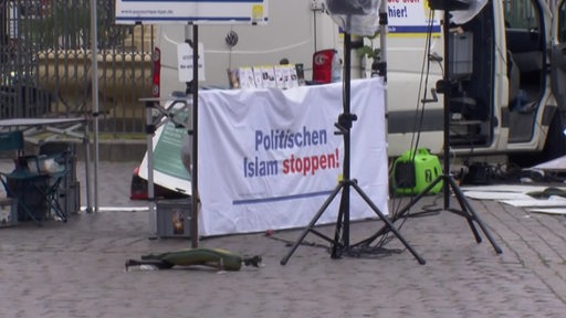 Auf einem Platz steht ein Stand, an welchem ein Plakat mit der Aufschrift "Politischen Isalam stoppen!" steht.