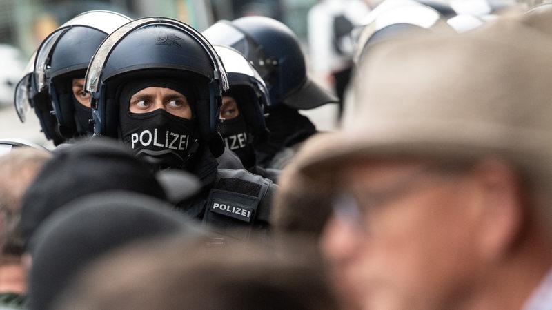 Beamte der Bundespolizei stehen mit Helmen und Sturmmasken zwischen Menschen