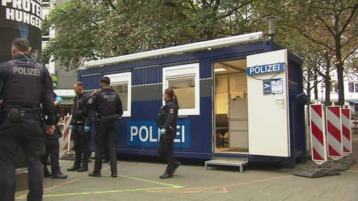 Mehrere Polizistinnen und Polizisten vor einem Polizeicontainer auf dem Hillmannplatz