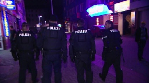 Vier Polizisten gehen eine dunkle Straße entlang