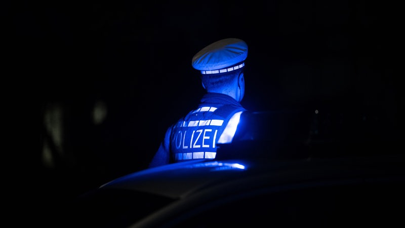 Ein Polizist in Uniform wird von Blaulicht angestrahlt.