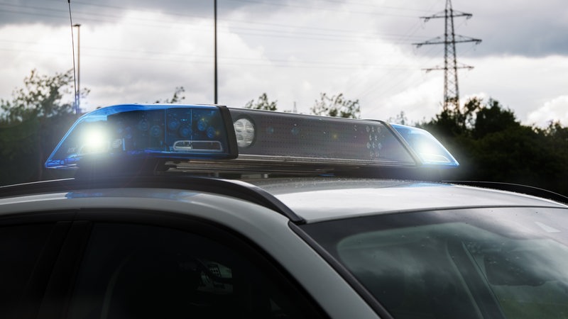 Auf einem Polizeiwagen blinken die Blaulichter. Im Hintergrund sind dunkle Wolken zu sehen.