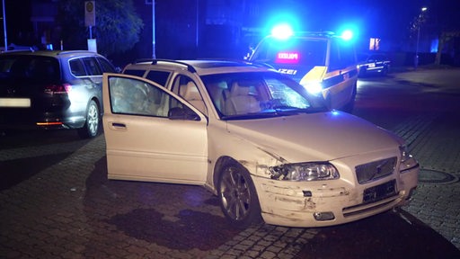 Ein an der Vorderseite beschädigter Volvo S80 steht vor einem Polizeiwagen mit Blaulicht