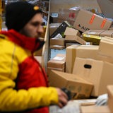 Ein Paketbote holt in einer Zustellbasis von DHL Pakete von einer Rutsche, um sie in seinen Transporter zu laden und seine Zustelltour zu beginnen.