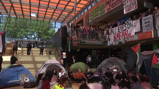 Ein Protestcamp mit einigen Menschen und Zelten im Glashaus der Uni bremen