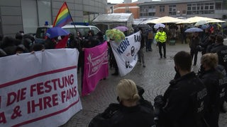 Mehrere Demonstrierende mit Schildern stehen gegenüber der Polizei in Delmenhorst, um gegen den Bürgerdialog der AfD zu protestieren.