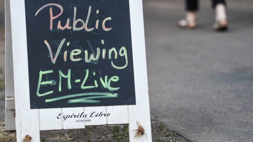 Vor einem Restaurant steht ein Schild mit der Aufschrift „Public Viewing EM-Live“.