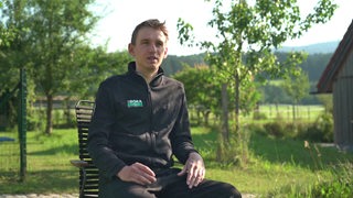 Lennard Kämna sitzt während des Interviews draußen auf einem Stuhl.Hinter ihm ist eine Berglandschaft zu sehen.