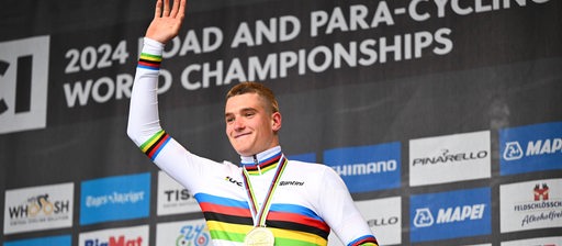 Der Bremer Radprofi Niklas Behrens winkt strahlend vom Podium mit der Goldmedaille um den Hals für seinen Titel bei der U23-WM.