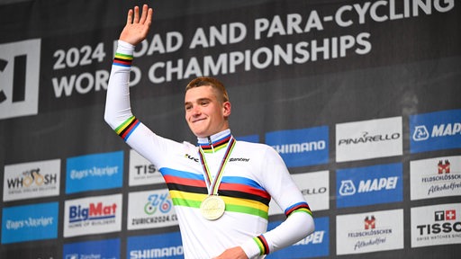 Der Bremer Radprofi Niklas Behrens winkt strahlend vom Podium mit der Goldmedaille um den Hals für seinen Titel bei der U23-WM.