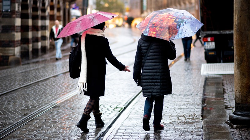 Zwei Frauen gehen bei regnerischem Wetter mit Regenschirmen über die Obernstraße im Stadtzentrum.