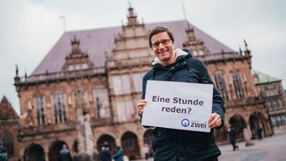 Ein Mann hält ein Schild auf dem steht: Eine Stunde reden