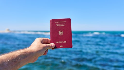 Ein Tourist hält Reisepass der Bundesrepublik Deutschland vor das Meer im Urlaub.