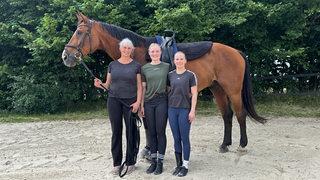 Die Voltigier-Reiterinnen Gisa Sternberg und Linda Otten stehen mit ihrer Trainerin Cornelia Ammermann vor ihrem Pferd Eddie.