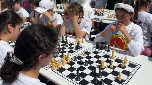 Mehrere Kinder spielen an Tischen Schach gegeneinander.