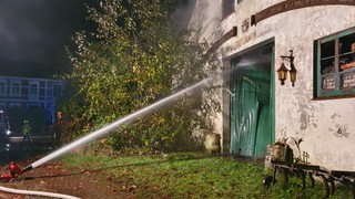 Aus einem Feuerwehrschlauch, der auf ein Scheunentor gerichtet ist, kommt ein Wasserstrahl.