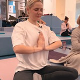 Eine Frau sitzt in Trainingsklamotten im Schneidersitz auf dem Boden und macht eine Yoga-Pose