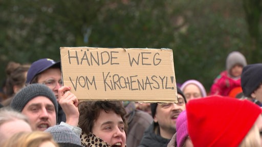 Auf einer Demonstration hält ein Schild hoch, auf dem die Einhaltung des Kirchenasyls gefordert wird