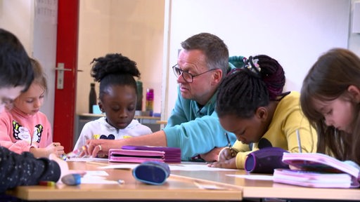 Ein Lehrer sitzt neben einigen Schülerinnen in einem Klassenzimmer.