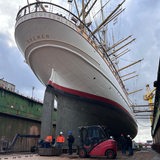 Menschen und ein Gabelstapler stehen unter einem Schiff im Dock.