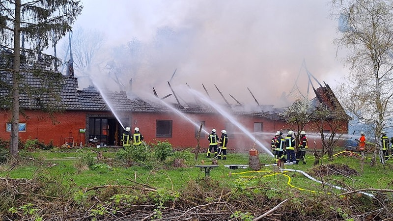 Mehrere Feuerwehrleute löschen einen Brand in einem Bauernhof.