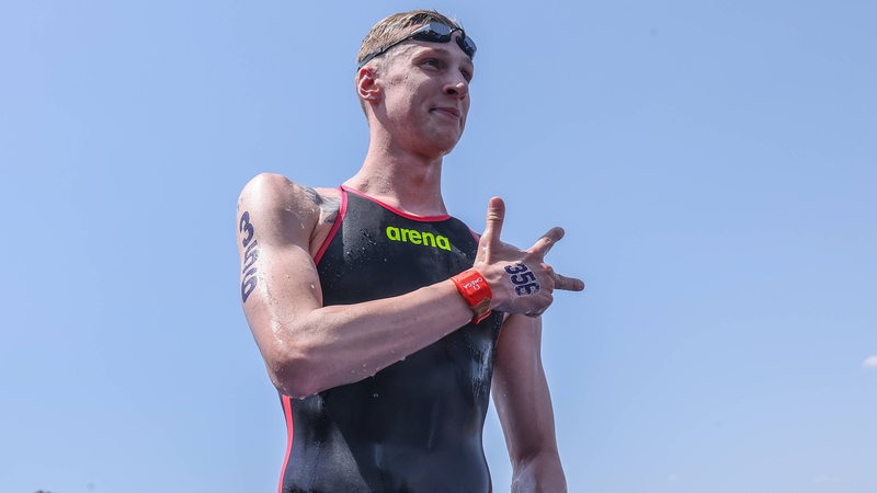 Schwimmstar Florian Wellbrock lächelt nach einem Wettkampf im Freiwasser und reckt drei Finger hoch.