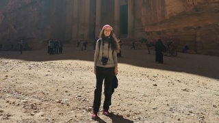 Eine Frau steht mit Spiegelreflexkamera vor einem Felsgebäude in Petra.