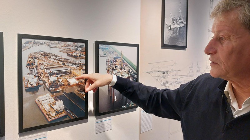 Ein Mann zeigt auf ein Hafen-Foto an der Wand.