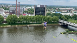 Eine Person hockt hoch oben auf einer Slackline über der Weser