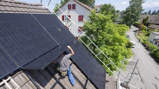 Ein Mann bei der Installation einer Solar und Photovoltankikanlage auf dem Dach eines Einfamilienhaus 