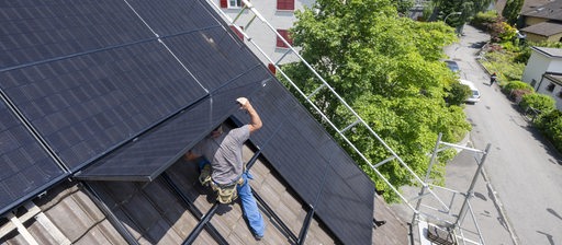 Ein Mann bei der Installation einer Solar und Photovoltankikanlage auf dem Dach eines Einfamilienhaus 