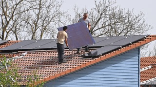 Einfamilienhaus mit Photovoltaikanlage:Arbeiter bei der Montage von Solarpanels auf einem Hausdach. Solarzellen,Solarmodule, Wohnhaus, Solarstrom,Solarenergie ?