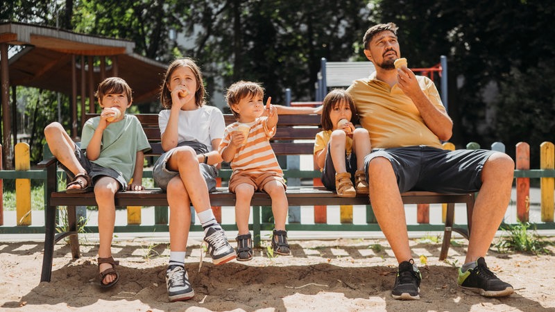 Familie sitzt mit einer Kugel Eis draußen auf einer Parkbank.